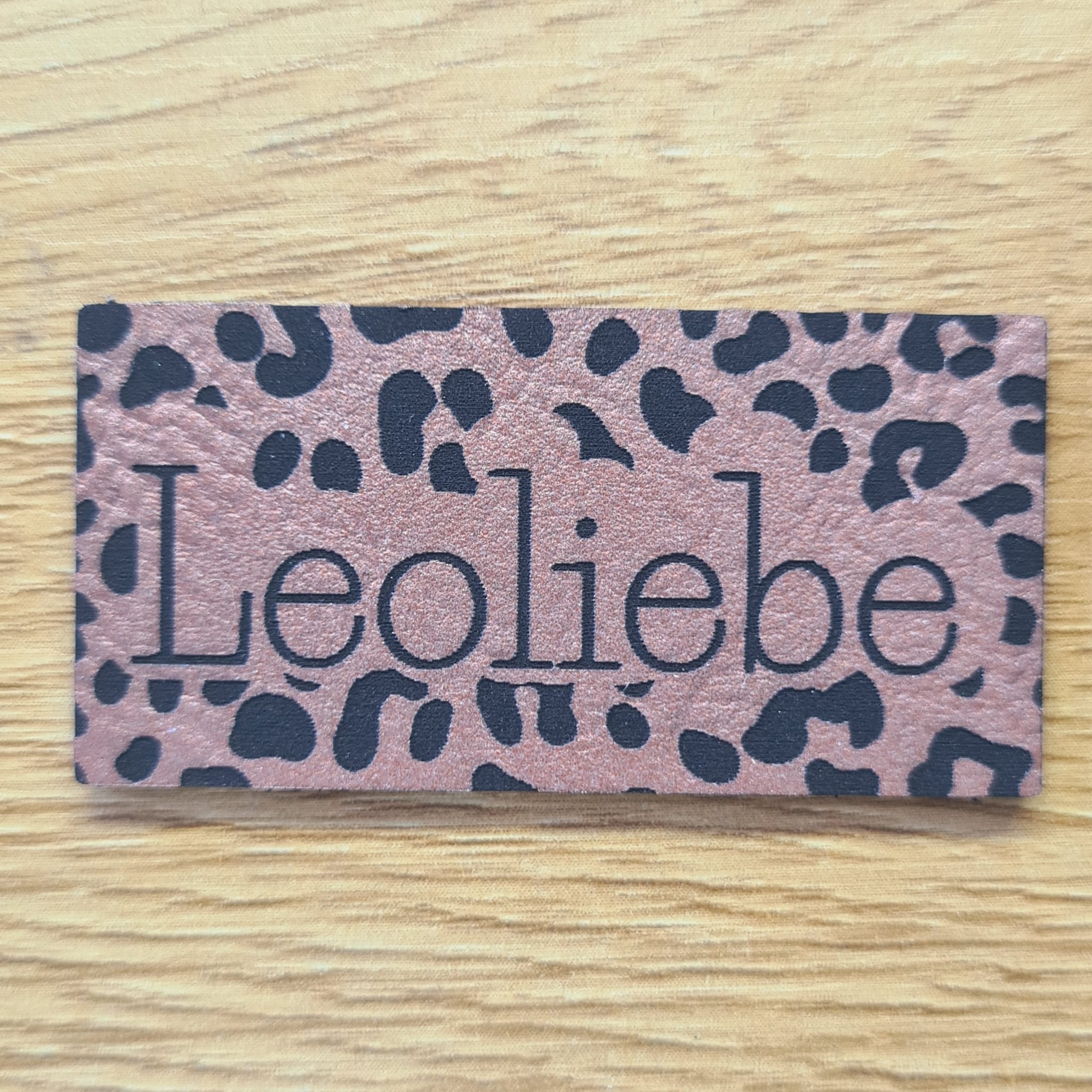 Rechteckiges rosegoldenes Kunstleder-Label mit dem gravierten Wort „Leoliebe“ und dezenten Leoparden-Punkten, 5,0 x 2,5 cm, veganes Nählabel für Taschen und Kleidung, laser-graviert bei Schnuckidu.