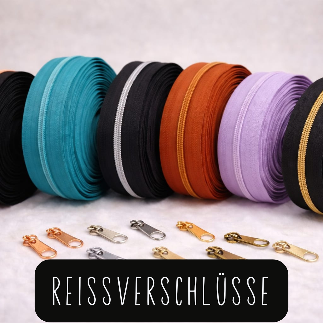 Mehrere aufgerollte Reißverschlüsse in verschiedenen Farben und dazu passende Reißverschluss-Schieber in Metallfarben auf hellem Untergrund