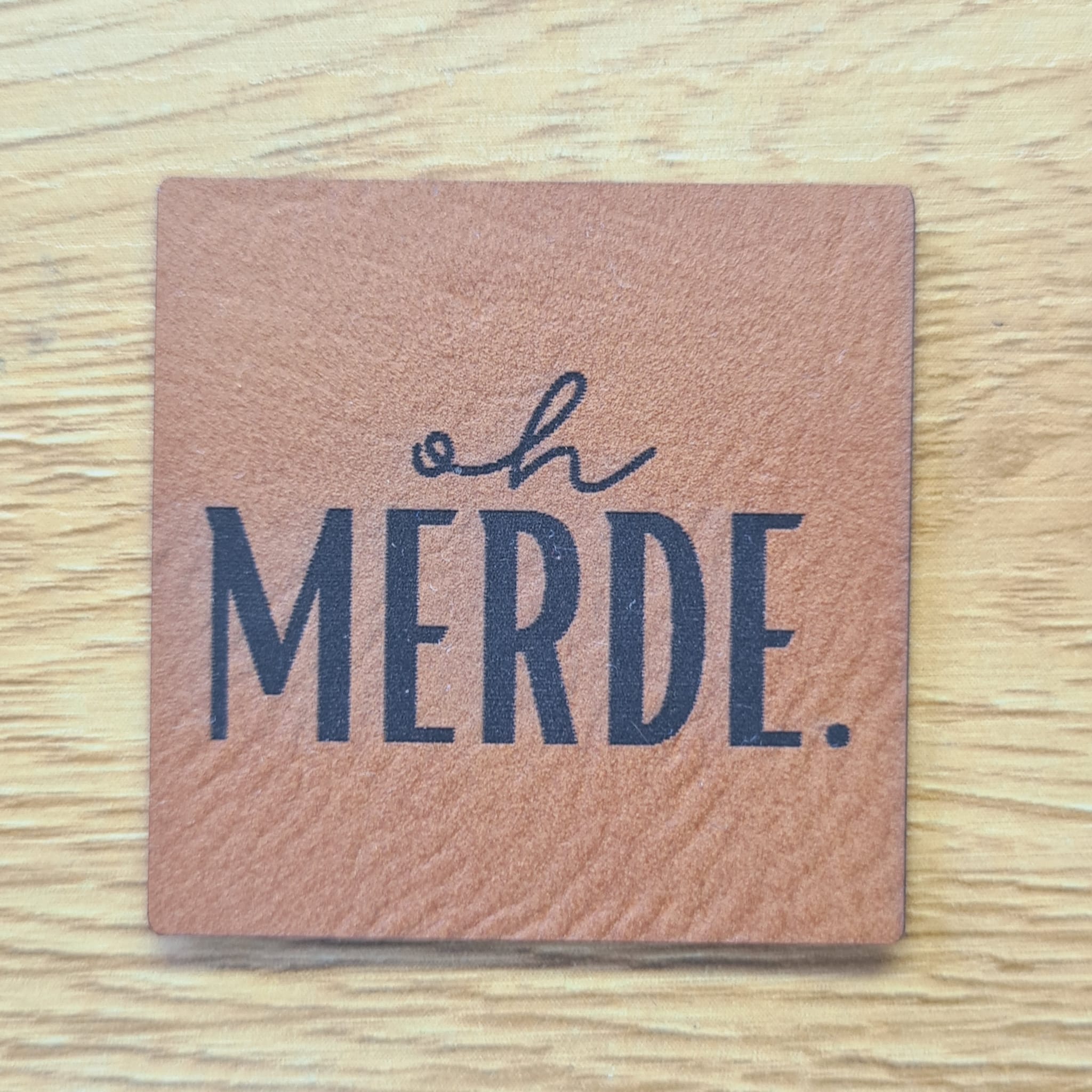 Quadratisches braunes Kunstleder-Label mit dem gravierten Spruch „oh MERDE.“, 4,0 x 4,0 cm, veganes Nählabel mit Humor für Streetwear, laser-graviert bei Schnuckidu.