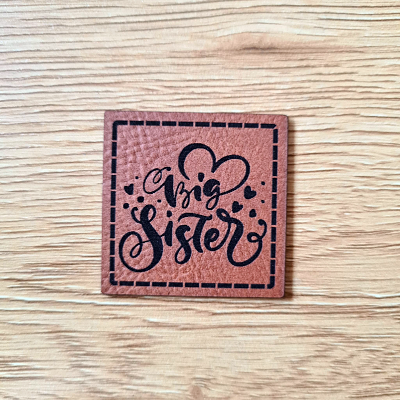 Quadratisches braunes Kunstleder-Label mit dem Schriftzug „Big sister“, 4 x 4 cm, veganes Nählabel für Geschwister-Outfits, laser-graviert bei Schnuckidu.