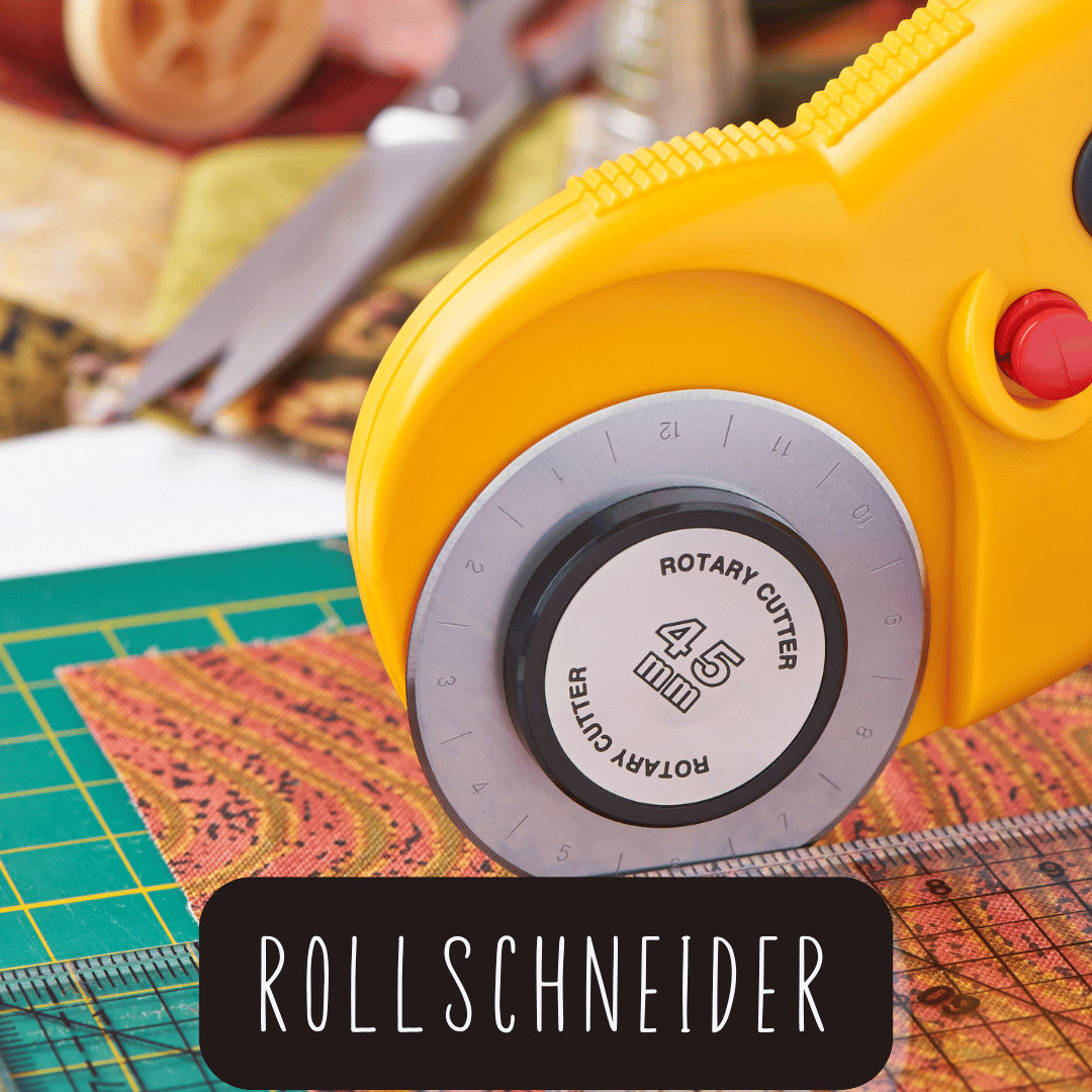 Nahaufnahme eines gelben Rollschneiders mit schwarzem Drehknopf und rotem Knopf auf einer Schneidematte mit Stoff und Schere im Hintergrund