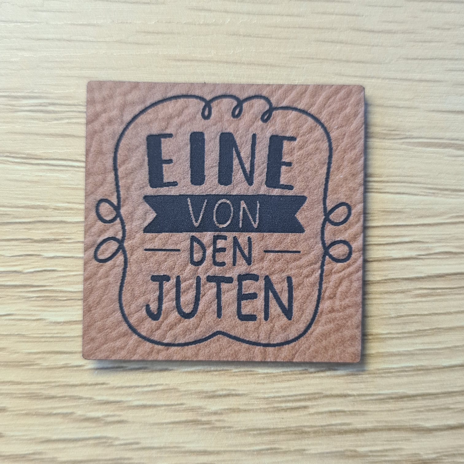 Schnuckidu Kunstleder Nählabel in Braun quadratisch mit Zierrahmen und dem Schriftzug Eine von den Juten.