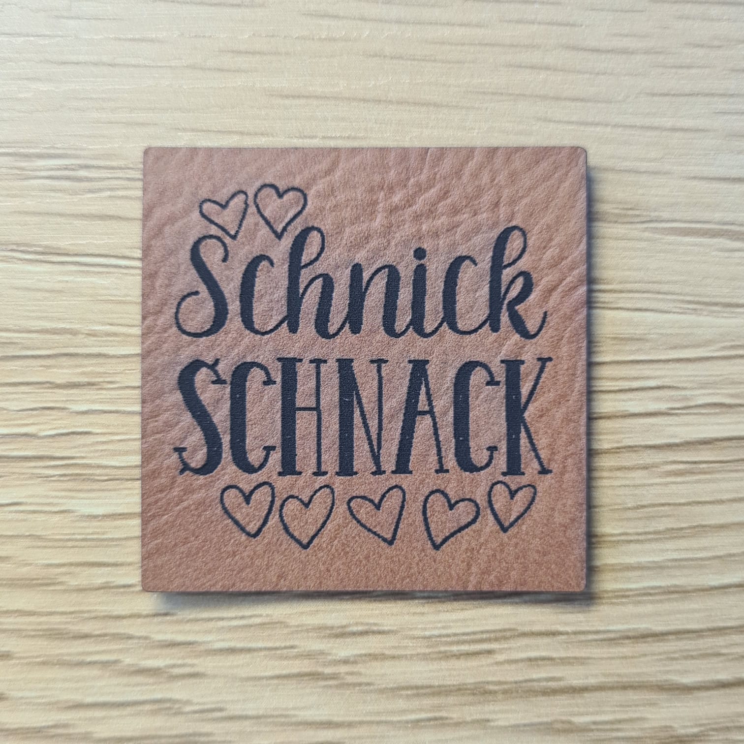 Schnuckidu Kunstleder Nählabel in Braun quadratisch mit dem Schriftzug Schnick Schnack und kleinen Herz-Illustrationen.