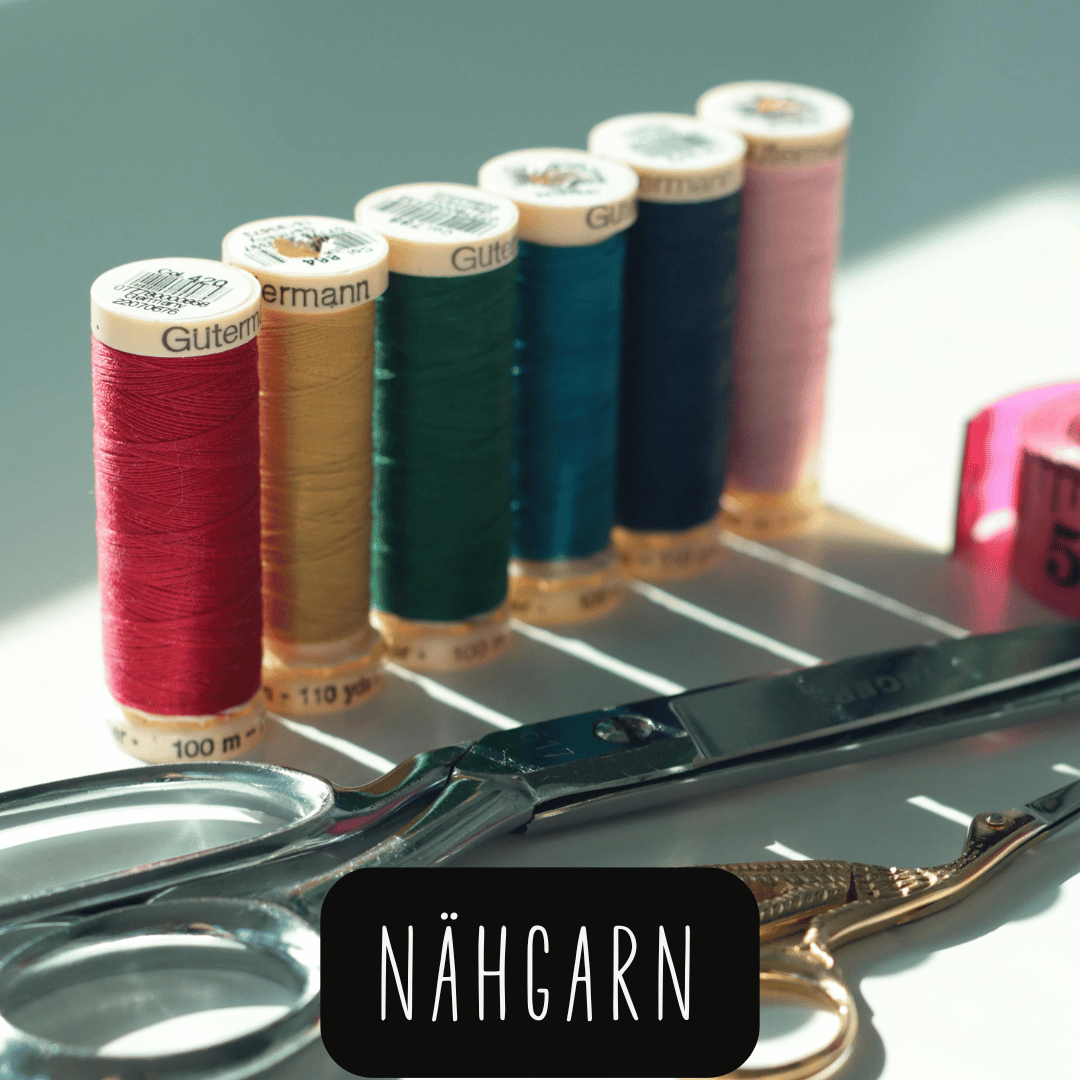 Mehrere bunte Garnspulen der Marke Gütermann hinter einer großen und einer kleinen Schere auf hellem Untergrund