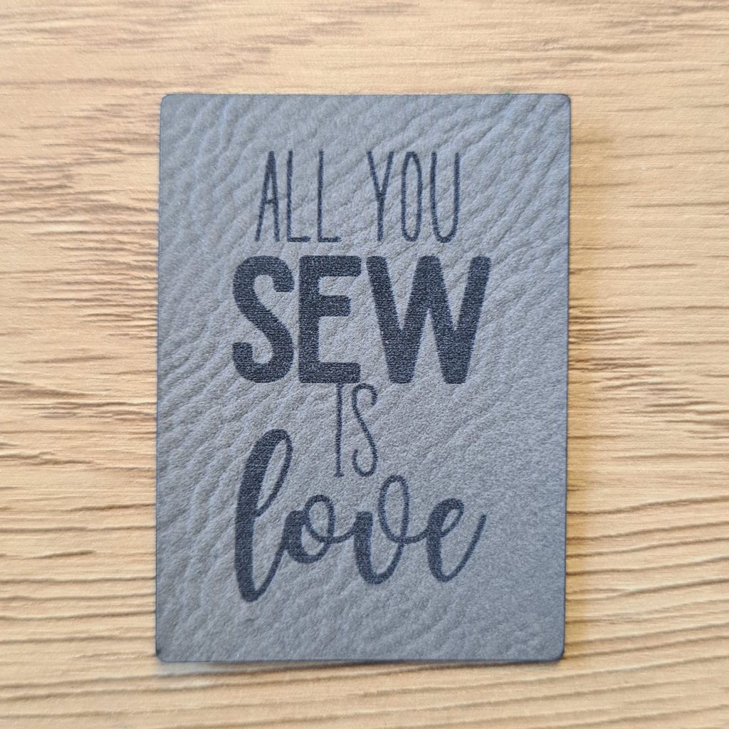 Rechteckiges graues Kunstleder-Label mit dem Spruch „All you sew is Love“, 3,6 x 5 cm, veganes Nählabel für mit Liebe genähte Kleidung und Accessoires, laser-graviert bei Schnuckidu.