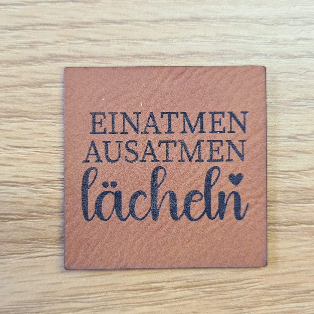 Quadratisches braunes Kunstleder-Label mit dem Spruch „Einatmen.Ausatmen.Lächeln“, ca. 4 x 4 cm, veganes Leder-Patch für Wellness- & Yoga-Projekte, laser-graviert bei Schnuckidu