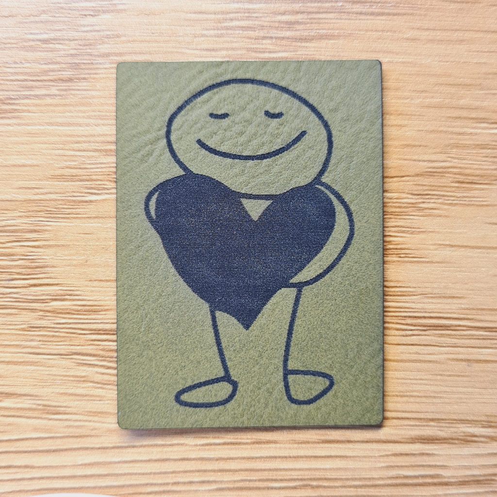 Rechteckiges olivegrünes Kunstleder-Label im Hochformat mit einem abstrakten Line-Art-Motiv einer Figur, die ein Herz hält, 3,1 x 5 cm, veganes Nählabel für moderne Kleidung, laser-graviert bei Schnuckidu.
