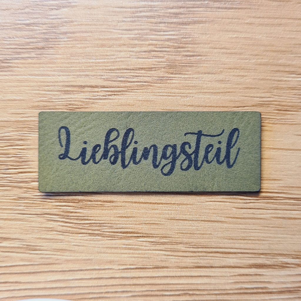 Schmales, rechteckiges olivegrünes Kunstleder-Label mit dem Schriftzug „Lieblingsteil“, 4,8 x 1,4 cm, veganes Nählabel für Kleidung und Accessoires, laser-graviert bei Schnuckidu.