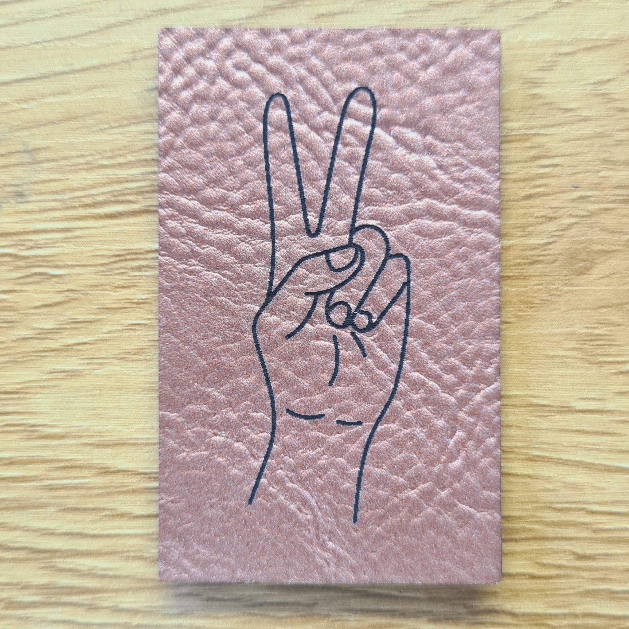 Hochkant-rechteckiges rosegoldenes Kunstleder-Label mit dem gravierten Wort „Peace“ und einem Peace-Zeichen, 3,0 x 5,0 cm, veganes Nählabel für Hoodies und Taschen, laser-graviert bei Schnuckidu.