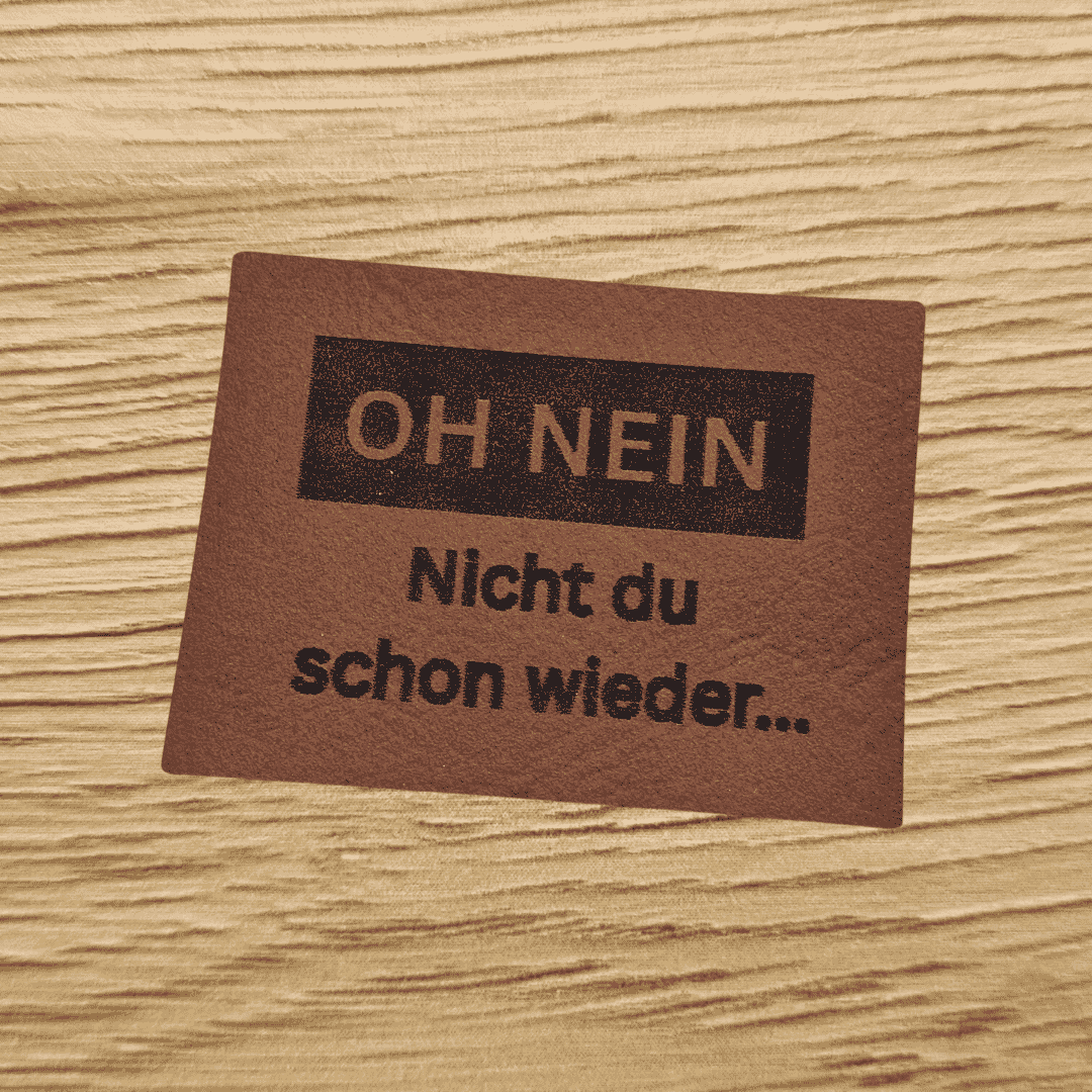 Rechteckiges braunes Kunstleder-Label mit dem gravierten Spruch „OH NEIN Nicht du schon wieder...“, bezugnehmend auf das Produktbild ohnein.png, veganes Nählabel für Kleidung und Accessoires, laser-graviert bei Schnuckidu.