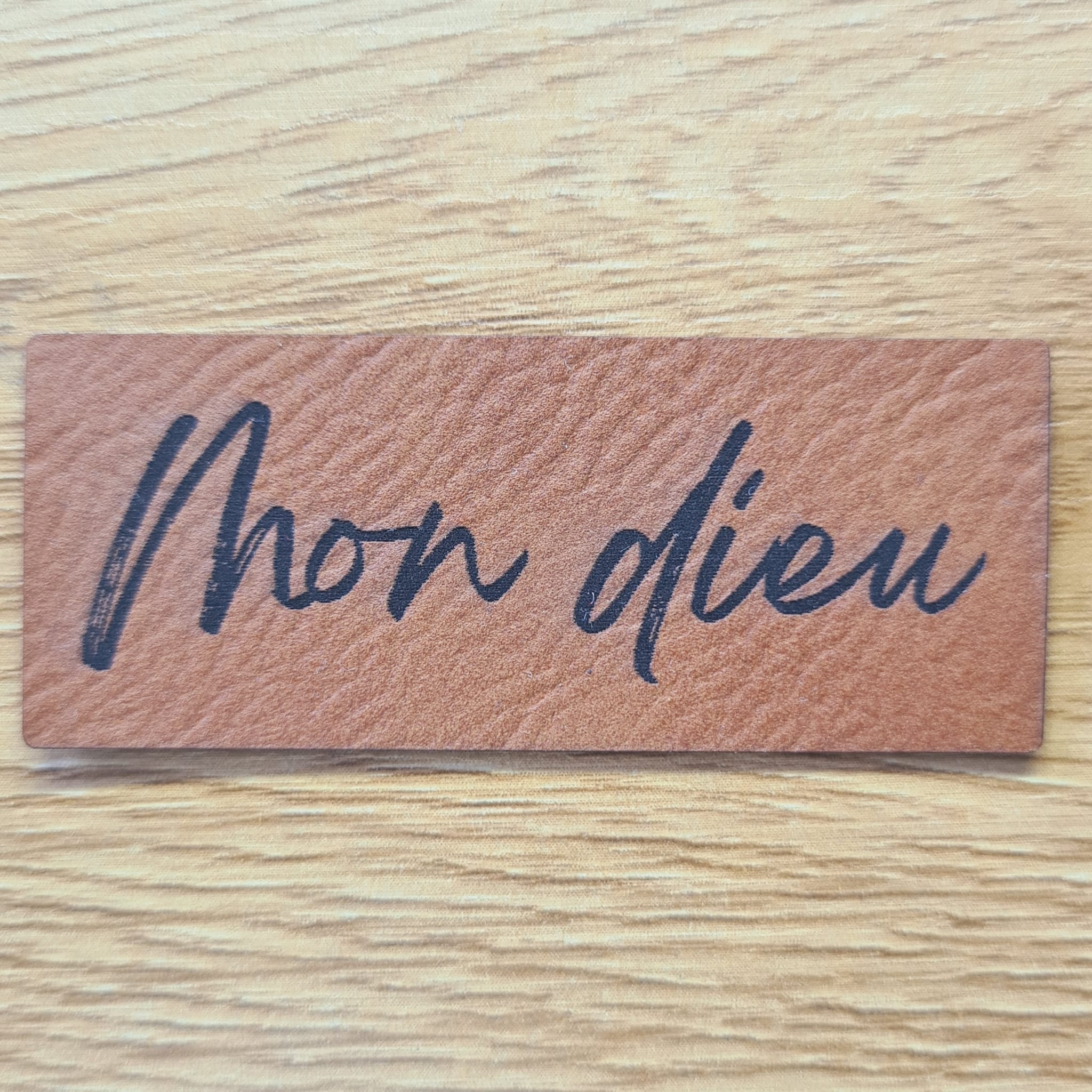 Rechteckiges braunes Kunstleder-Label mit dem gravierten Schriftzug „Mon dieu“, 6,0 x 2,4 cm, veganes Nählabel für Kleidung und Taschen, laser-graviert bei Schnuckidu.