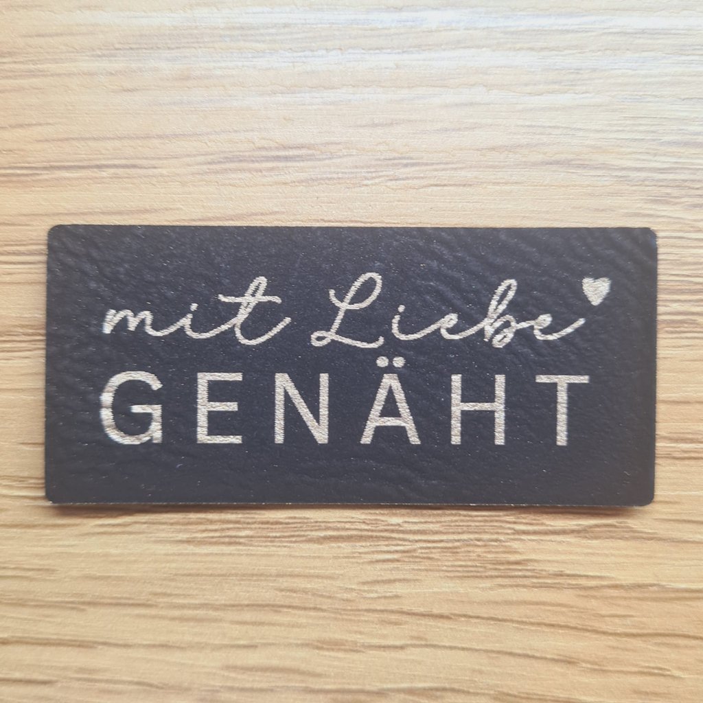 Schwarzes Kunstleder-Label mit goldener Aufschrift „Mit Liebe genäht“ und Herz-Symbol, ca. 6 x 2,7 cm, veganes Leder-Patch, laser-graviert bei Schnuckidu