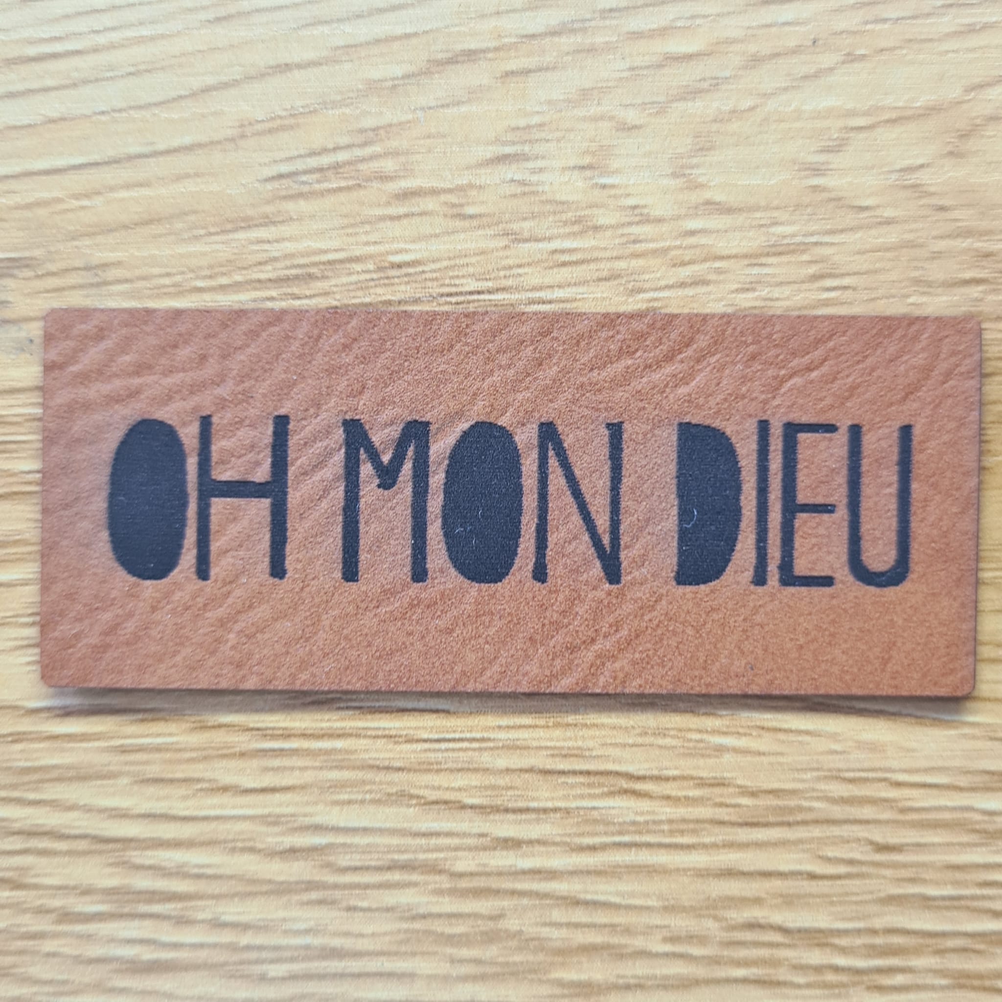 Rechteckiges braunes Kunstleder-Label mit dem gravierten Schriftzug „OH MON DIEU“, 6,0 x 2,4 cm, veganes Nählabel für Kleidung und Taschen, laser-graviert bei Schnuckidu.