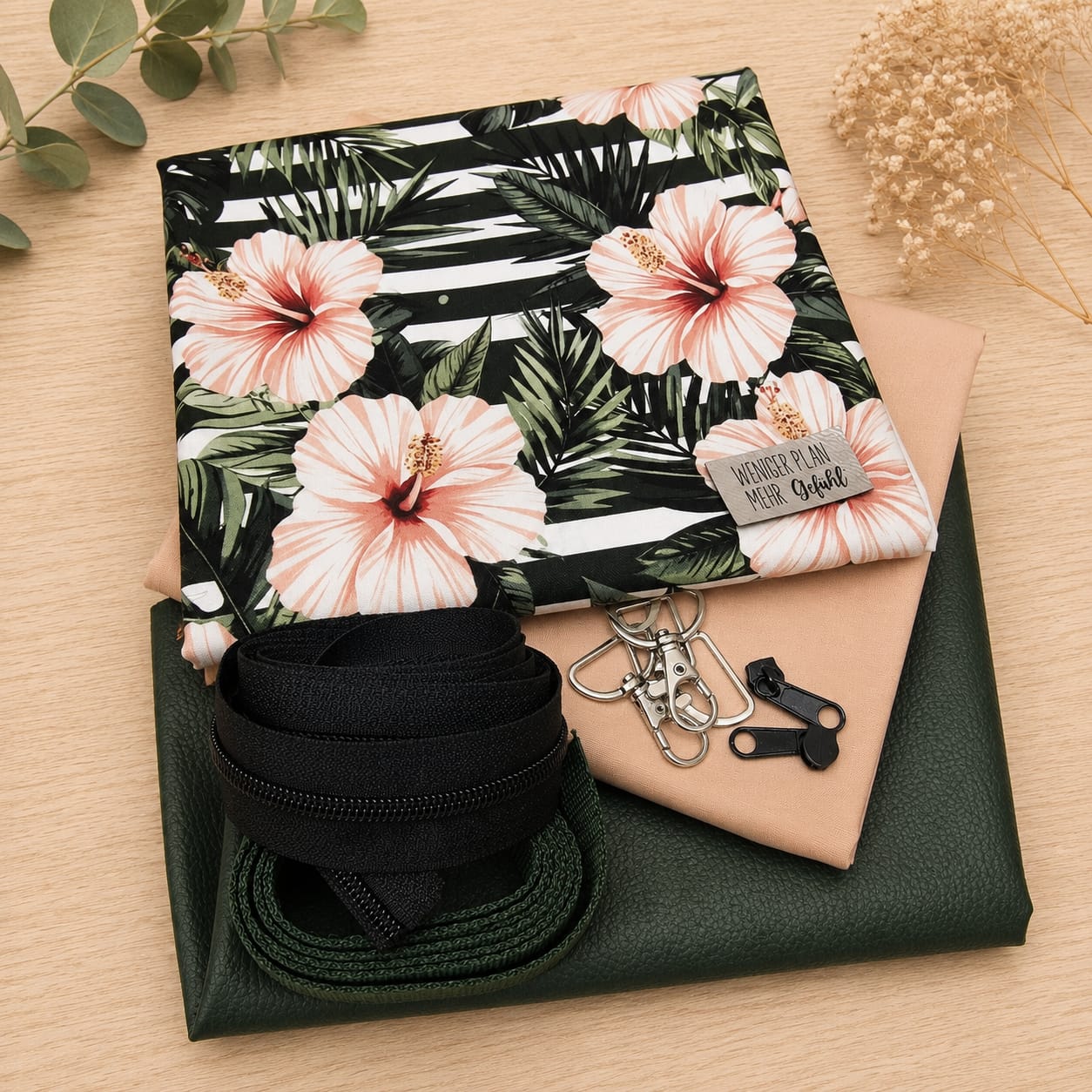 Schnuckidu Taschen-Stoffpaket Tropical Flowers mit gestreifter Hibiskus-Webware, pfirsichfarbenem Kombistoff, tannengrünem Kunstleder, dunkelgrünem Gurtband, silbernen Karabinern und grauem Kunstleder-Label "Weniger Plan, mehr Gefühl".