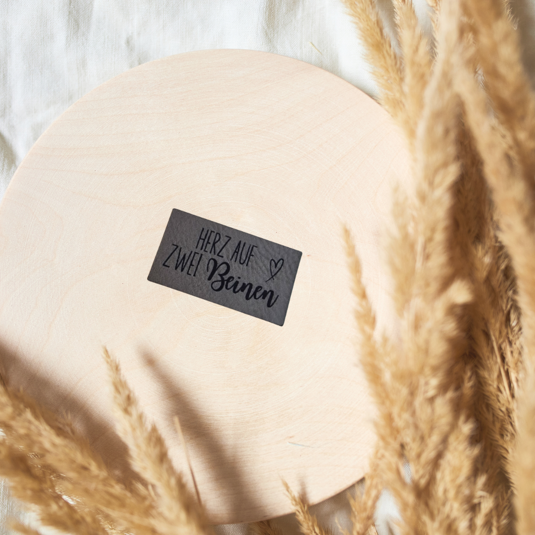 Rechteckiges graues Kunstleder-Label mit dem Schriftzug „Herz auf zwei Beinen“, 4,2 x 2,3 cm, veganes Nählabel für Baby- und Kinderkleidung, laser-graviert bei Schnuckidu.