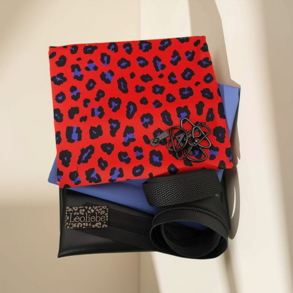 Stoffpaket Taschenpaket Leo rot mit rot-blauem Leo-Muster Canvas, unifarbenem blauen Canvas, schwarzem Kunstleder, schwarzem Gurtband, Karabiner-Set, Reißverschluss und einem Leoliebe-Label.