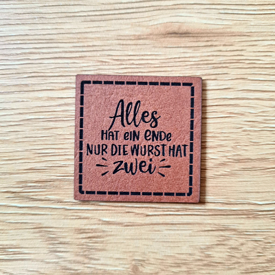 Quadratisches Kunstleder-Label mit dem Spruch „Alles hat ein Ende, nur die Wurst hat 2“, 4 x 4 cm, Braun mit schwarzer Gravur, veganes Nählabel, laser-graviert bei Schnuckidu.