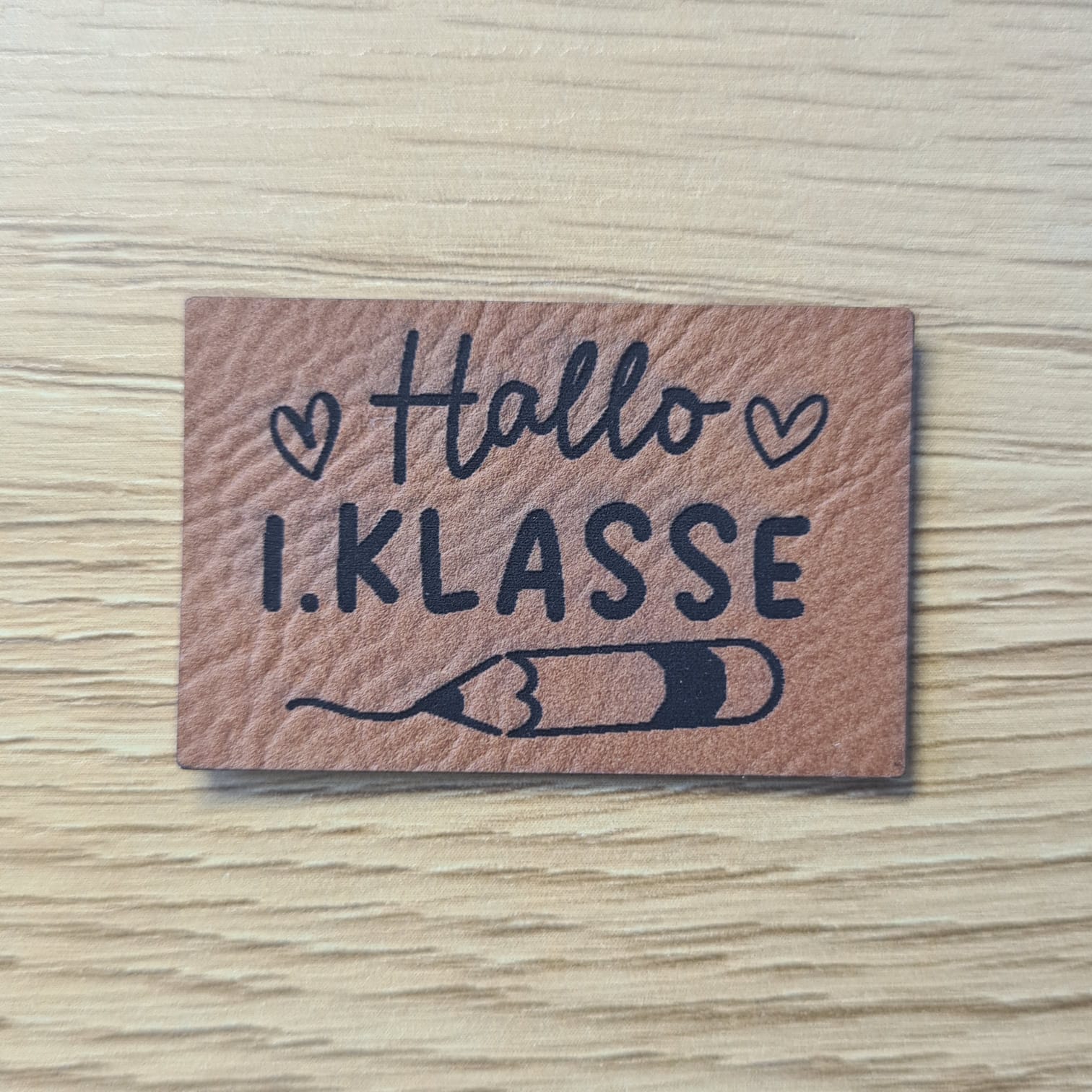 Schnuckidu Kunstleder Nählabel in Braun mit Schriftzug Hallo 1. Klasse, Herzen und Stift-Motiv.