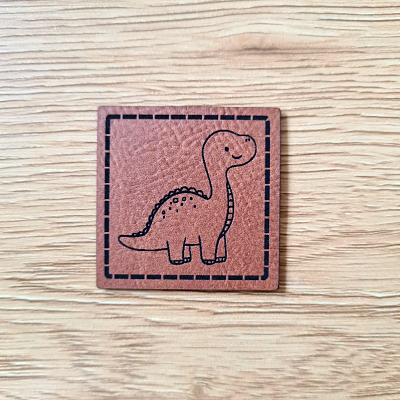 Quadratisches Kunstleder-Label mit niedlichem Baby-Dinosaurier-Motiv, 4 x 4 cm, Braun mit schwarzer Gravur, veganes Nählabel für Kinderkleidung, Schnuckidu.