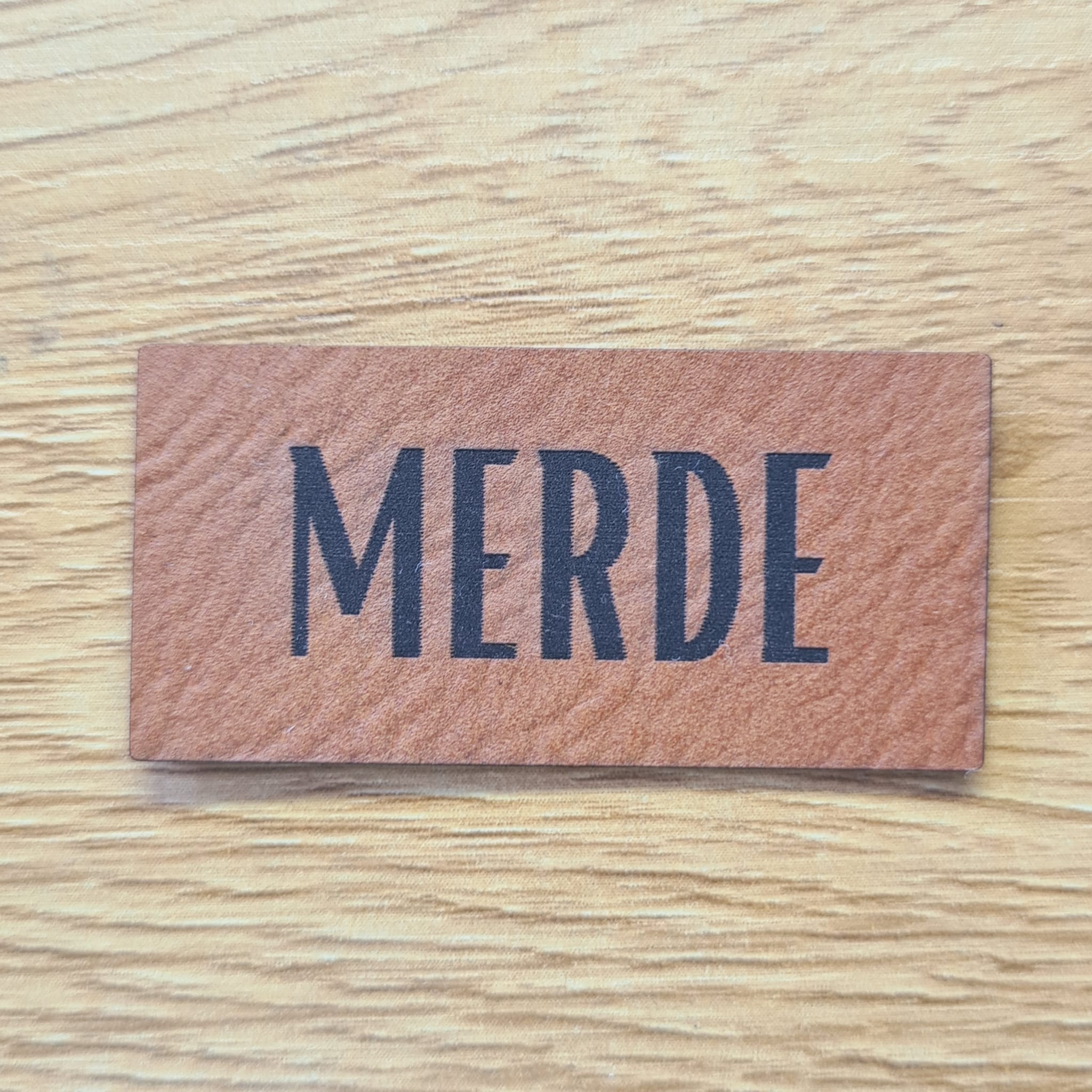 Rechteckiges braunes Kunstleder-Label mit dem gravierten Wort „MERDE“, 4,5 x 2,2 cm, veganes Nählabel mit Humor für Kleidung und Taschen, laser-graviert bei Schnuckidu.