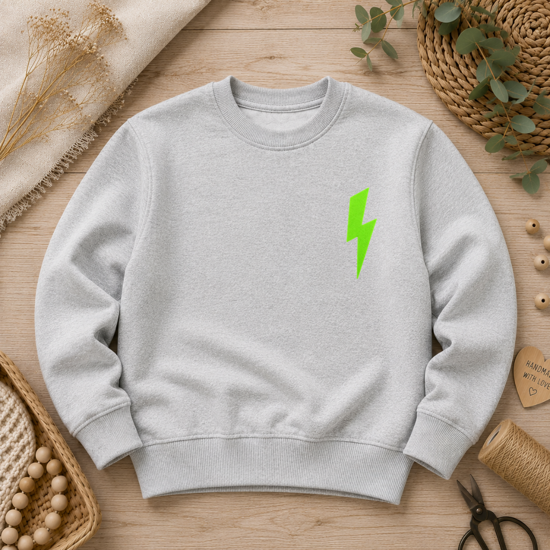 Samtiges Flock-Patch in Form eines vertikalen Blitzes in Neon-Grün aufgebügelt auf der Brust eines grauen Sweatshirts.