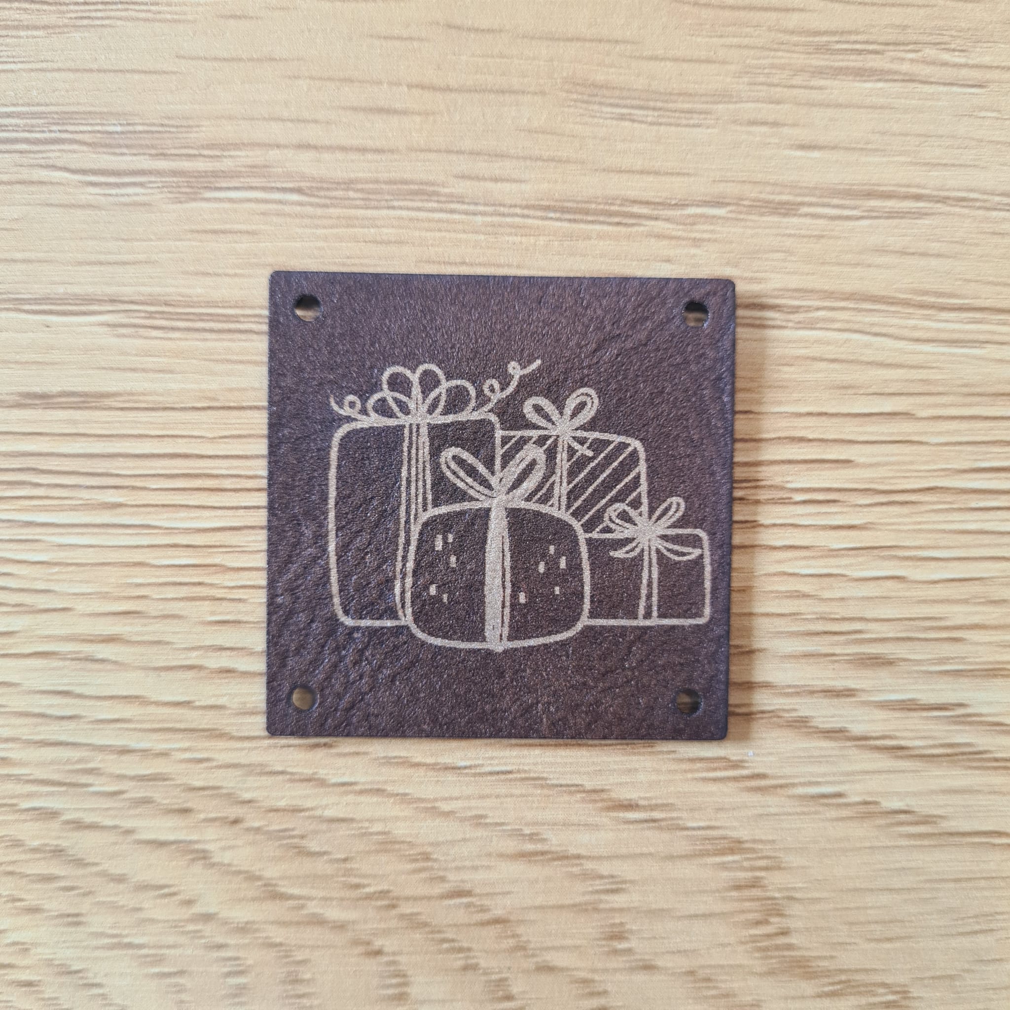 Quadratisches Kunstleder-Label mit Geschenke-Motiv, 4 x 4 cm, Braun mit Gold-Gravur, veganes Näh-Label für Präsente, laser-graviert bei Schnuckidu.