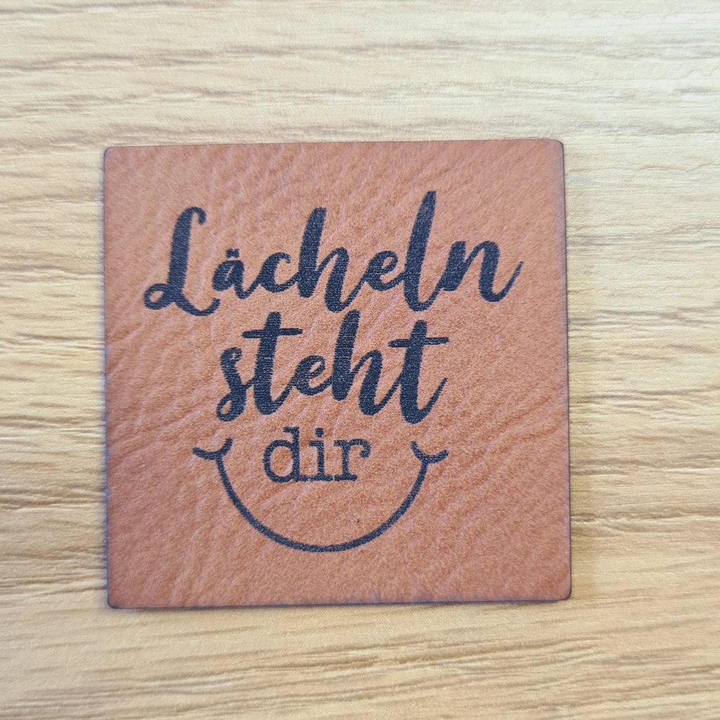 Quadratisches braunes Kunstleder-Label mit dem Spruch „Lächeln steht dir gut“, ca. 4 x 4 cm, veganes Leder-Patch mit Kompliment, laser-graviert bei Schnuckidu