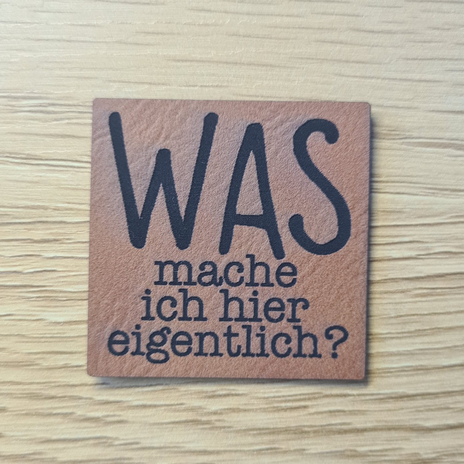 Schnuckidu Kunstleder Nählabel in Braun quadratisch mit dem humorvollen Schriftzug Was mache ich hier eigentlich.