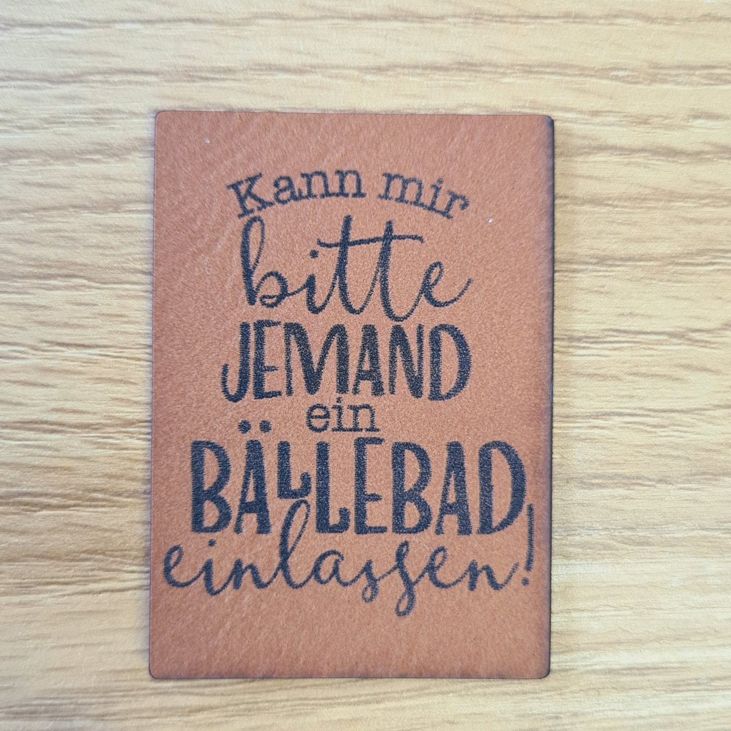 Hochformatiges braunes Kunstleder-Label mit dem Spruch „Kann mir bitte jemand ein Bällebad einlassen?“, ca. 3,8 x 5 cm, veganes Leder-Patch mit Humor, laser-graviert bei Schnuckidu