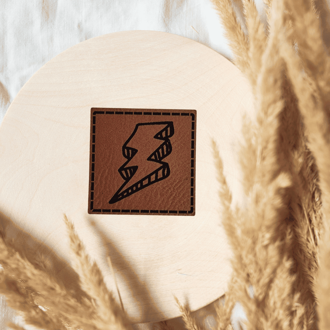 Quadratisches braunes Kunstleder-Label mit einem Blitz-Motiv, 4 x 4 cm, veganes Nählabel für coole Kinderkleidung und Streetwear, laser-graviert bei Schnuckidu.