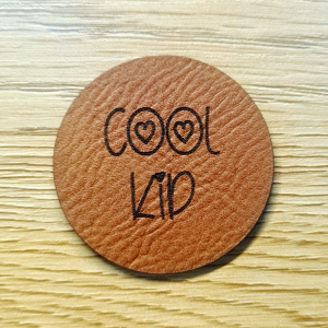 Rundes braunes Kunstleder-Label mit dem Schriftzug „Cool Kid“ und kleinen Sternen, ca. 4 cm Durchmesser, veganes Leder-Patch, laser-graviert bei Schnuckidu