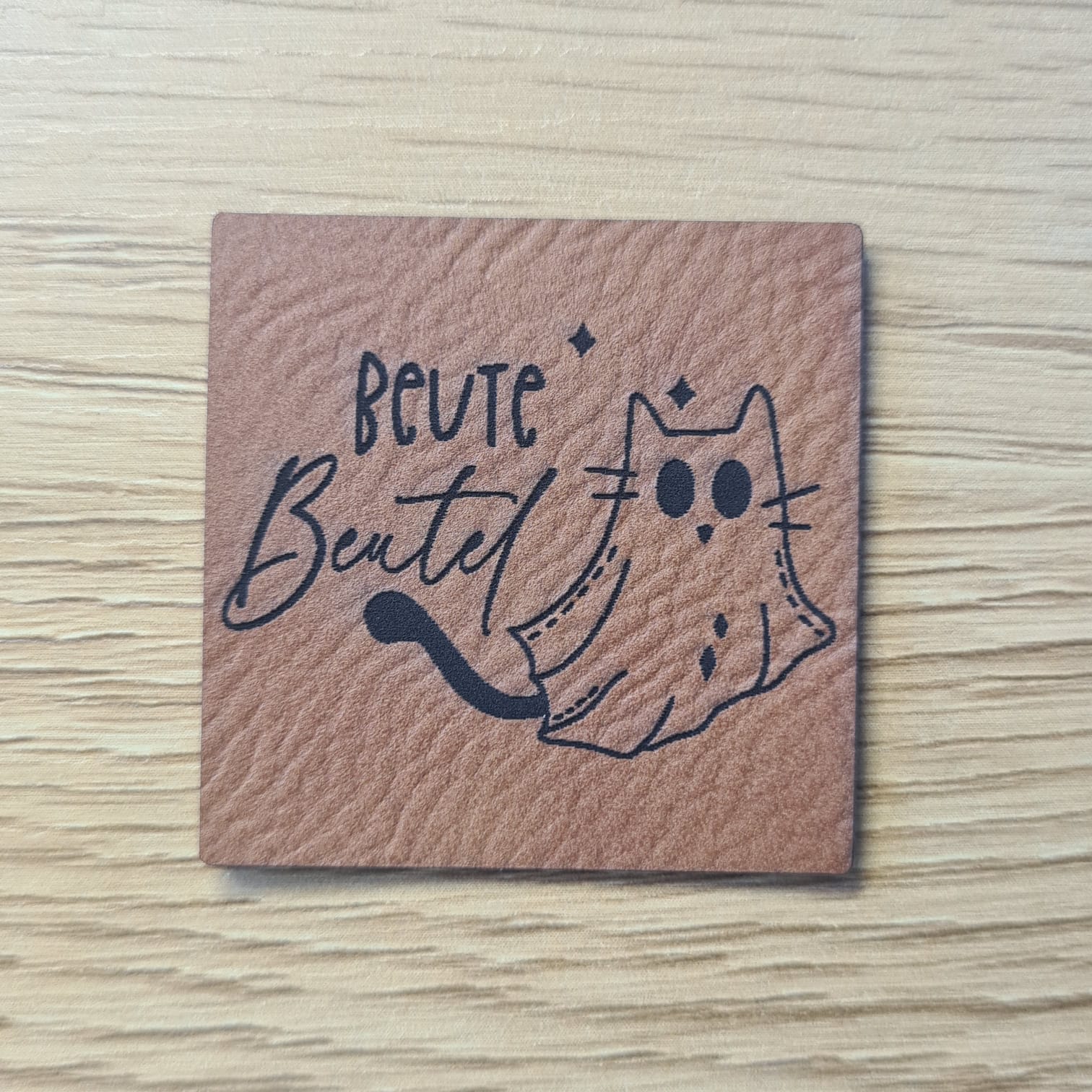 Schnuckidu Kunstleder Nählabel in Braun quadratisch mit einer Geisterkatze und dem Schriftzug Beute Beutel.