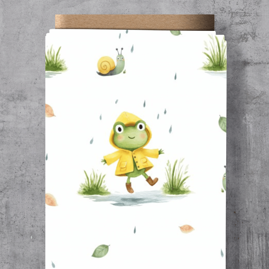 Süßer Kinderstoff mit dem Schnuckidu-Eigendesign „Regenfrosch“ – drollige Frösche mit bunten Regenschirmen, Gummistiefeln und kleinen Regentropfen im verspielten Allover-Muster.