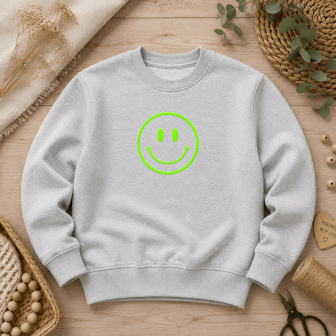 Flauschiges Flock-Patch Smiley in Neon-Grün mittig aufgebügelt auf der Brust eines grauen Kinder-Pullovers.