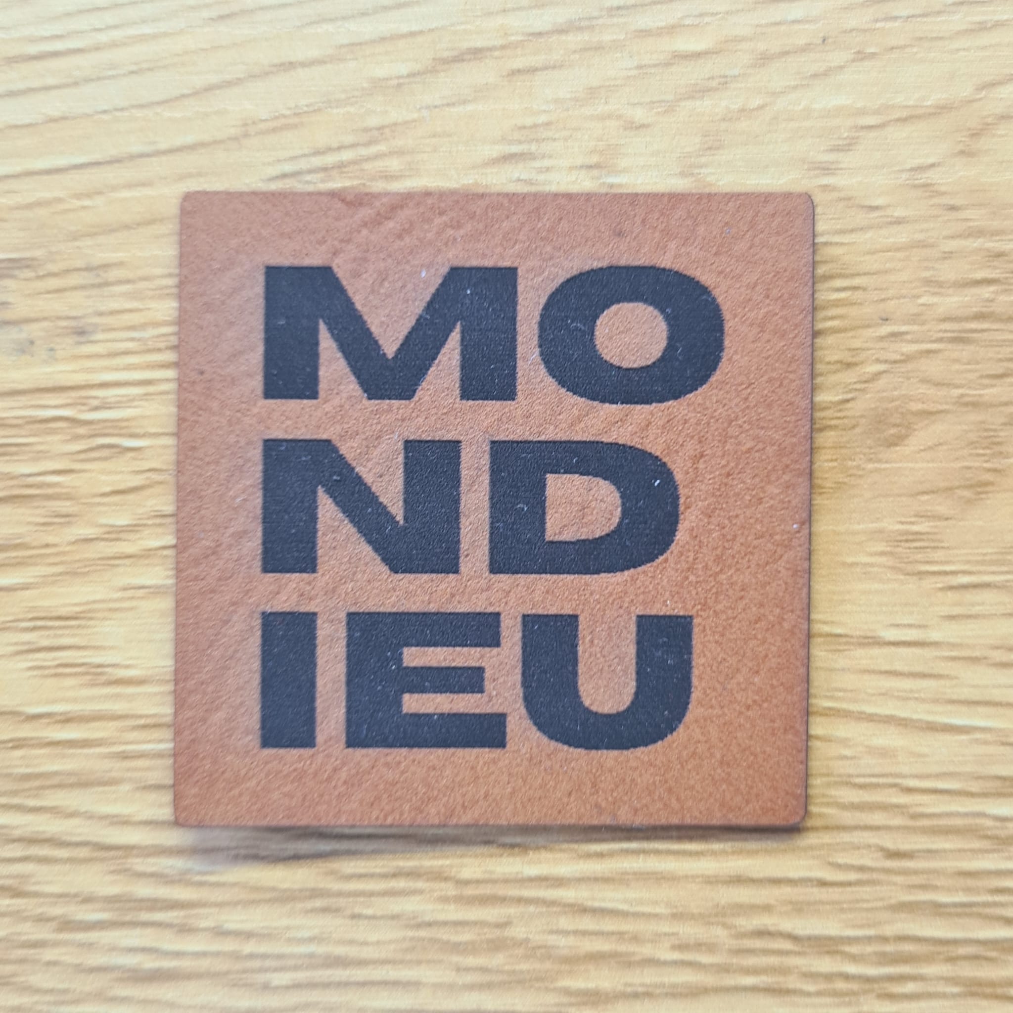 Quadratisches braunes Kunstleder-Label mit dem gravierten Schriftzug „MONDIEU“, 4,0 x 4,0 cm, veganes Nählabel für Streetwear und Taschen, laser-graviert bei Schnuckidu.