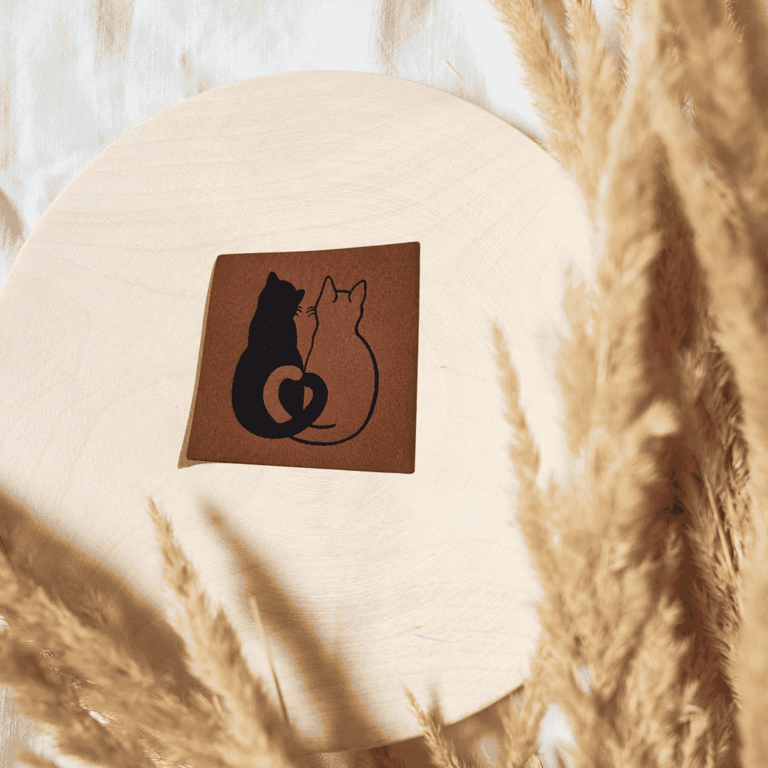 Quadratisches braunes Kunstleder-Label mit einem schmusenden Katzenpaar-Motiv, 4 x 4 cm, veganes Nählabel für Tierfreunde, laser-graviert bei Schnuckidu.