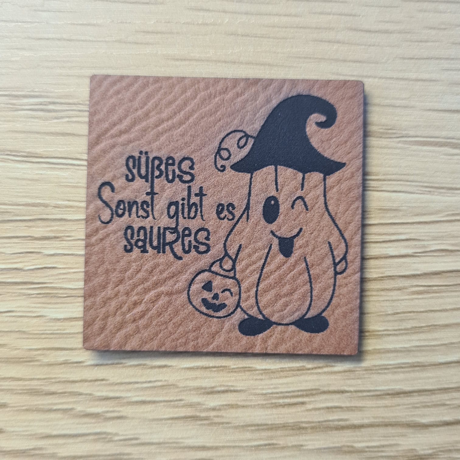Schnuckidu Kunstleder Nählabel in Braun quadratisch mit kleinem Geist im Hexenhut und Kürbiseimer sowie Schriftzug Süßes sonst gibt es Saures.