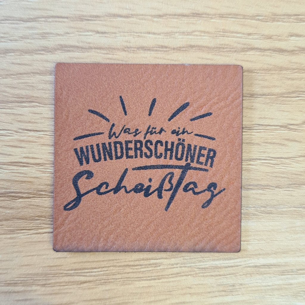 Quadratisches braunes Kunstleder-Label mit dem Spruch „Was für ein wunderschöner Scheißtag?“, ca. 4 x 4 cm, veganes Leder-Patch mit Humor, laser-graviert bei Schnuckidu